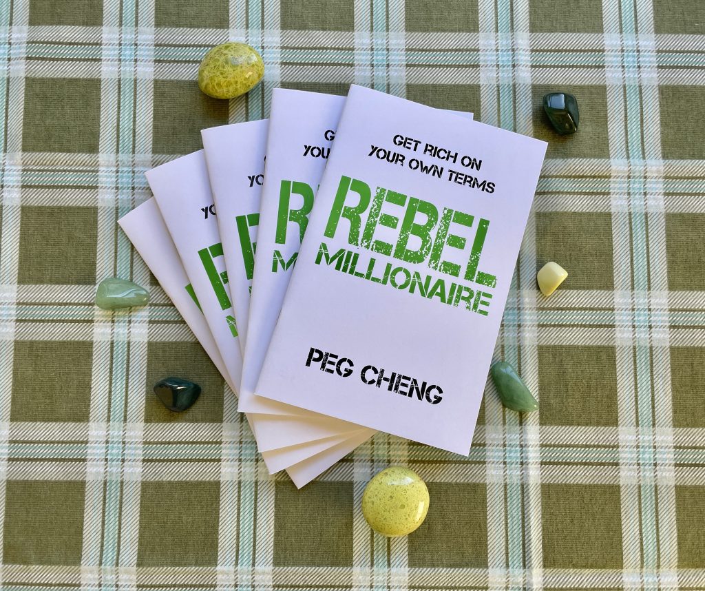 Stack of Rebel Millionaire zines on a green plaid fabric surrounded by green-colored stones